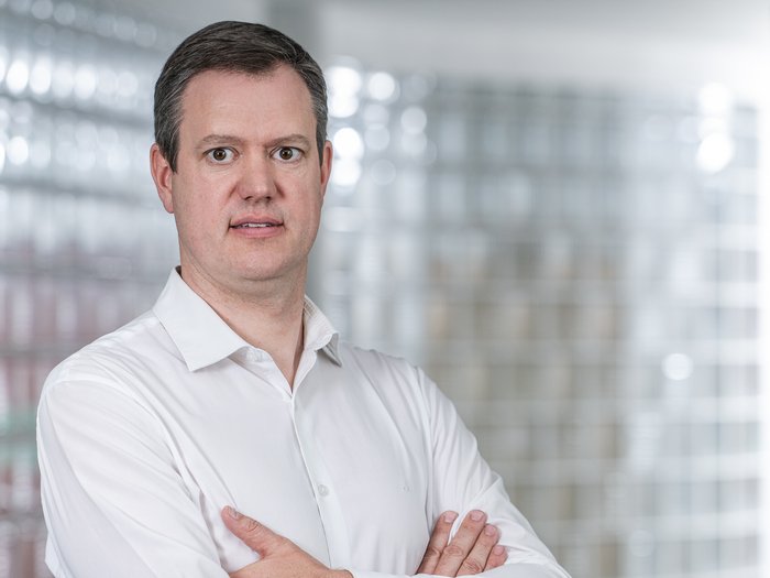 Arbeitssicherheit: Neue Maßnahmen müssen praxisnah und differenziert sein Mann mit weißem Hemd steht mit verschränkten Armen vor verglaster Wand