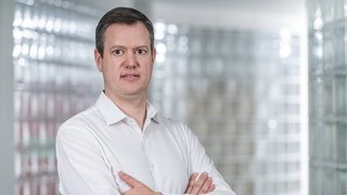 News Mann mit weißem Hemd steht mit verschränkten Armen vor verglaster Wand