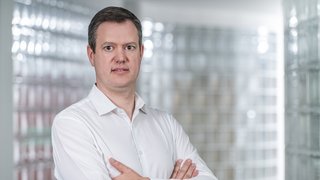 News Mann mit weißem Hemd steht mit verschränkten Armen vor verglaster Wand