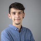 Manuel Pircher Junger Mann mit blauem Hemd und Ohrpiercing lächelt vor grauem Hintergrund