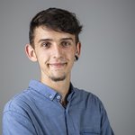 Das lvh-Team Junger Mann mit blauem Hemd und Ohrpiercing lächelt vor grauem Hintergrund