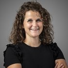 dott.ssa mag. Mirjam Kienzl Ritratto di donna sorridente con capelli ricci e maglietta nera su sfondo grigio