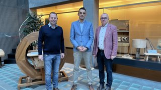 © lvh.apa Drei Männer stehen in einem modernen Raum mit Holzkunstwerken und Glasboden