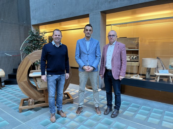 © lvh.apa Drei Männer stehen in einem modernen Raum mit Holzkunstwerken und Glasboden