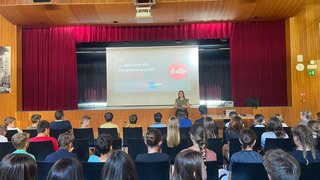 News Jugendliche hören auf einer Bühne einer Präsentation in einem Saal zu