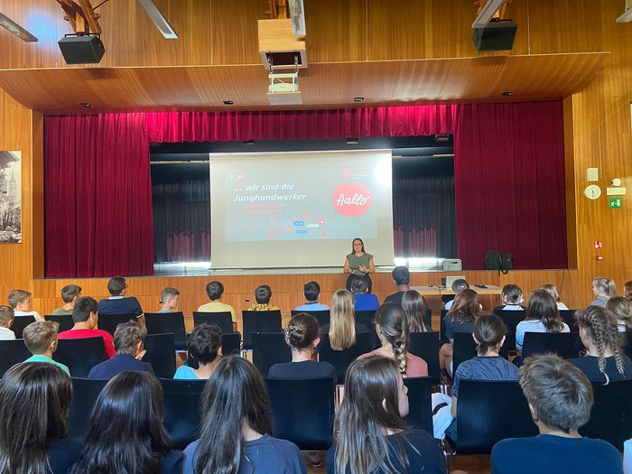 Eintauchen in die Welt der Berufe in Jenesien Jugendliche hören auf einer Bühne einer Präsentation in einem Saal zu