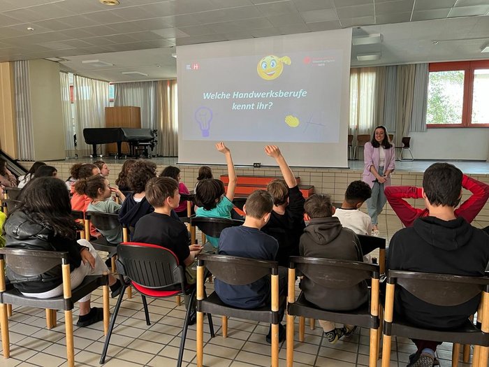 „Mit unseren Ausbildungen ist vieles möglich!“ Schüler heben Hände in einem Klassenzimmer vor einer Präsentation über Handwerksberufe