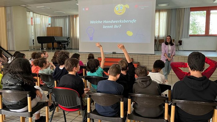 „Mit unseren Ausbildungen ist vieles möglich!“ Schüler heben Hände in einem Klassenzimmer vor einer Präsentation über Handwerksberufe