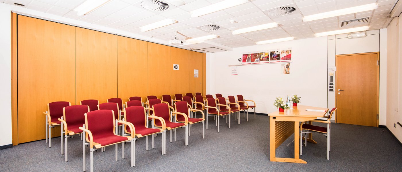 Vermietung Seminarräume Leerer Konferenzraum mit roten Stühlen und einem Tisch vorne