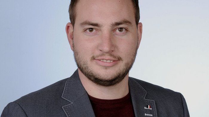Tiefbauer beklagen untragbare Treibstoffpreise Porträt eines Mannes mit dunkelblauem Sakko und rotem Pullover vor hellblauem Hintergrund