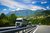 Camion percorrono autostrada davanti a paesaggio montano con cielo azzurro e nuvole