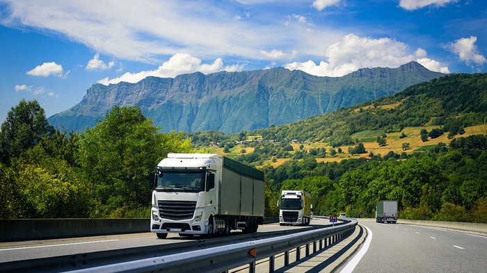 La delegazione altoatesina ha visitato il Talentcenter di Graz Camion percorrono autostrada davanti a paesaggio montano con cielo azzurro e nuvole