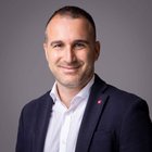 Arbeitsrecht & Gewerkschaftsfragen Porträt eines lächelnden Mannes in weißem Hemd und dunkelblauem Sakko vor grauem Hintergrund