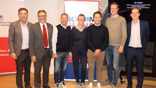 News Sieben Personen stehen vor zwei Rollup-Bannern und einem Bildschirm