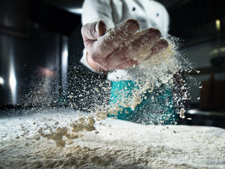 Panettieri Cuoco lancia farina in aria in cucina professionale