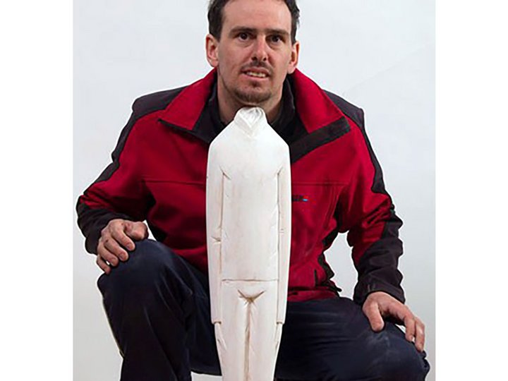 Ivan Art Mann kniet neben einer großen weißen Holzfigur einer stehenden Person