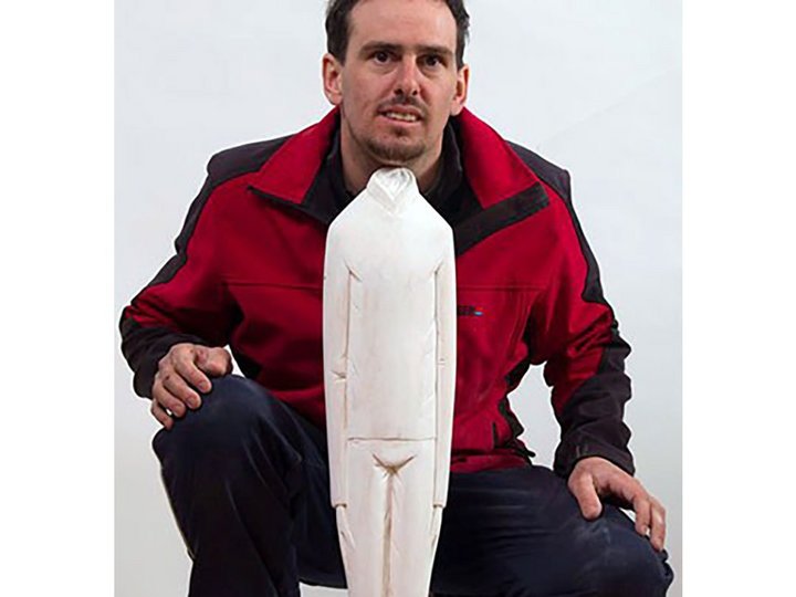 Ivan Art Mann kniet neben einer großen weißen Holzfigur einer stehenden Person