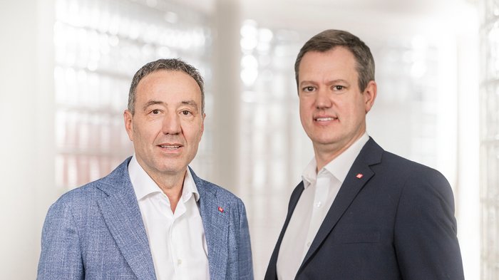 Südtirols Betriebe als stille Leistungsträger der Winterspiele Zwei Männer in Anzügen vor hellem, unscharfem Hintergrund