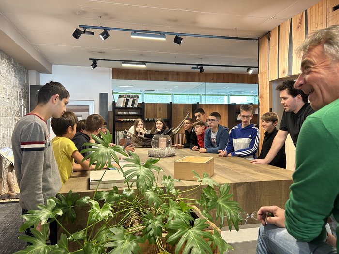 Die Handwerks- und Gastbetriebe von Bozen im Fokus Gruppe von Jugendlichen und Erwachsenen um einen großen Holztisch versammelt in modernem Raum