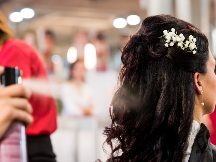 Friseure Frau erhält Haarspray auf kunstvoll gestyltes dunkles Haar mit weißen Blumen