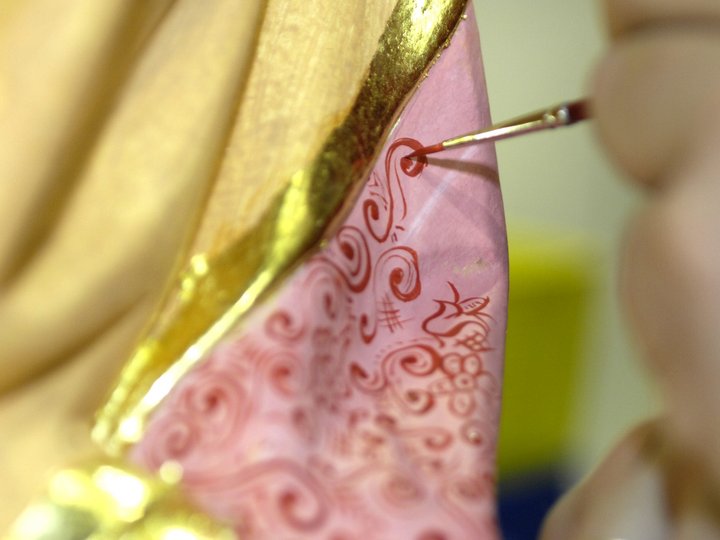 Policromatori e doratori Primo piano di una mano che dipinge motivi rossi su una superficie rosa