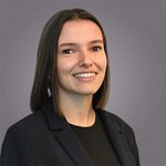 Das lvh-Team Porträt einer lächelnden Frau mit braunen Haaren und dunklem Blazer vor grauem Hintergrund