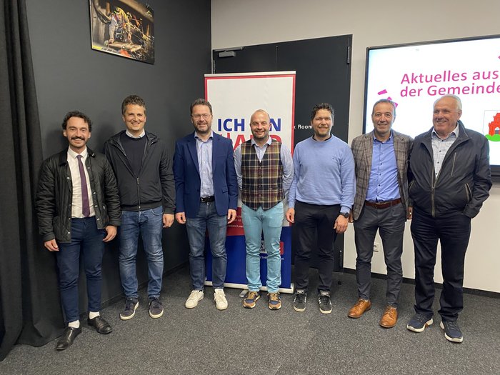 Solides Handwerk in Bruneck Sieben Männer stehen nebeneinander vor Werbebannern und lächeln in die Kamera