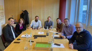 News Acht Personen bei einer Besprechung an einem Konferenztisch in einem Büro