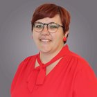 Julia Ranigler MBA Ritratto di donna con camicetta rossa e occhiali su sfondo grigio