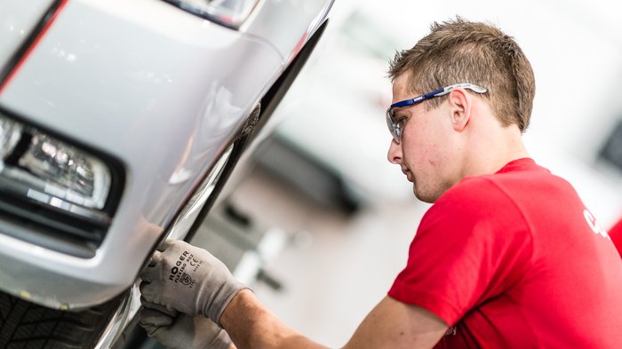 Kfz-Mechatroniker erinnern an Winterreifenpflicht Mechaniker prüft Reifenzustand an einem silbernen Auto mit Schutzbrille