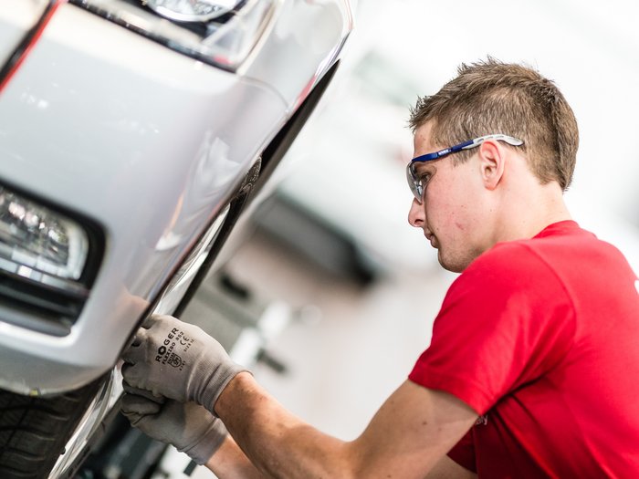 Kfz-Mechatroniker erinnern an Winterreifenpflicht Mechaniker prüft Reifenzustand an einem silbernen Auto mit Schutzbrille