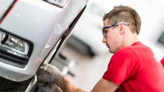 News Mechaniker prüft Reifenzustand an einem silbernen Auto mit Schutzbrille