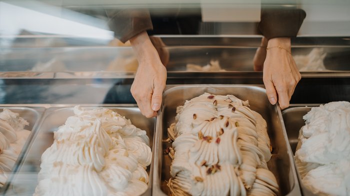 "Gambero Rosso": premiata la gelateria AiJOO Mani che tengono una vaschetta di gelato al pistacchio nel congelatore