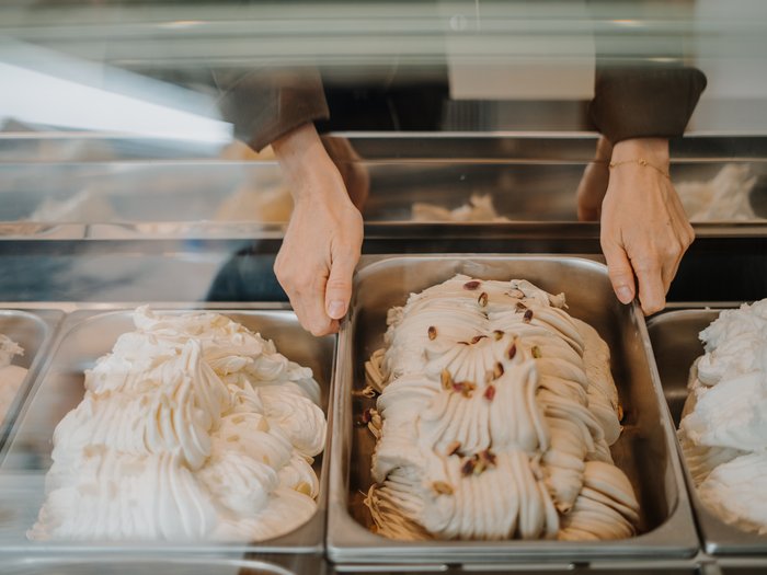 "Gambero Rosso": premiata la gelateria AiJOO Mani che tengono una vaschetta di gelato al pistacchio nel congelatore