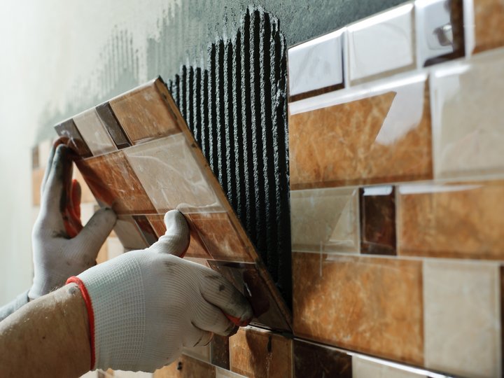 Fliesen-, Platten- und Mosaikleger Hände mit Handschuhen, die an einer Wand Fliesen anbringen