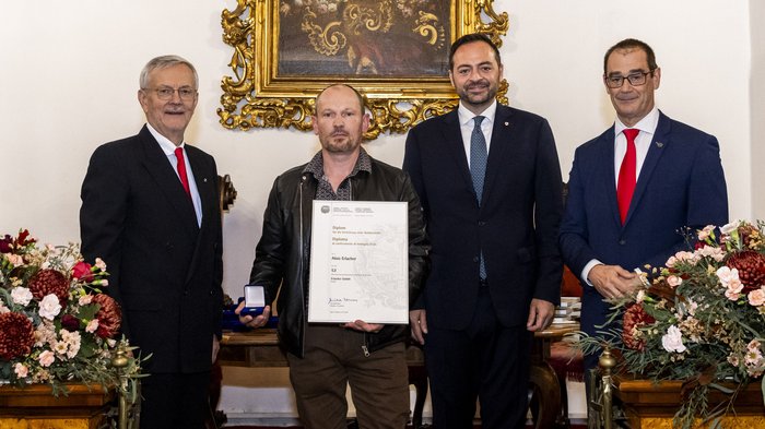 Südtiroler Wirtschaftspreis 2024 Vier Männer bei Preisverleihung, einer hält Urkunde und Medaille