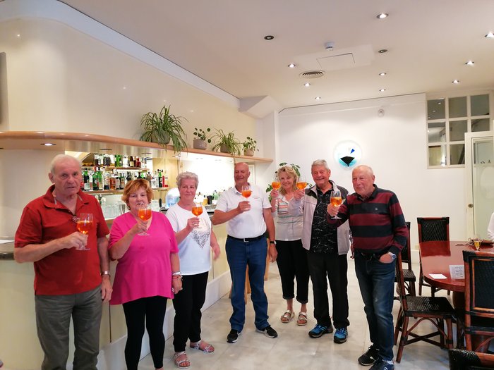 Badespaß an der Adria Gruppe von Senioren, die mit Aperol-Spritz in einem hellen Barraum anstoßen
