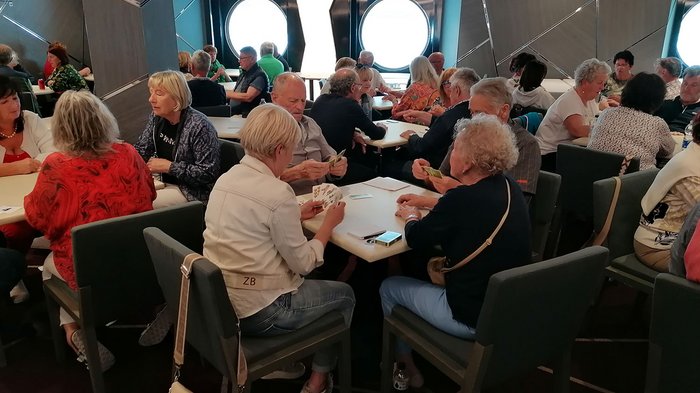 Artigiani anziani in crociera Anziani che giocano a carte a più tavoli in una stanza con oblò