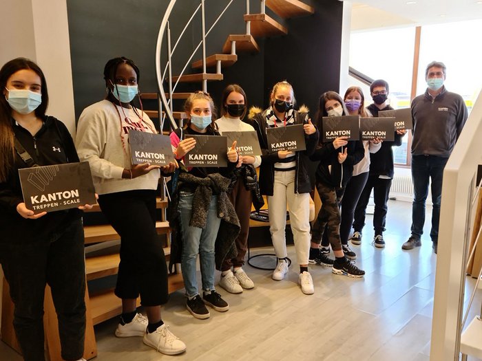 Mittelschule Neumarkt besichtigt Handwerksbetriebe und Hotels in Montan, Tramin und Auer Gruppe von Personen mit Masken hält Kanton Treppen Scale Schilder in modernem Innenraum