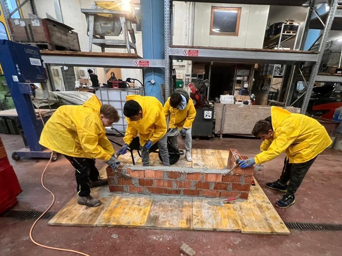 Berufsinformationskampagne in Deutschnofen und Welschnofen Vier Personen in gelben Jacken mauern eine Ziegelsteinwand in einer Werkstatt