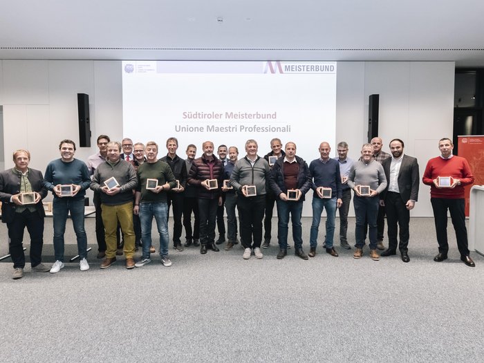 © Alan Bianchi Gruppenfoto von 20 Männern mit Auszeichnungen vor Südtiroler Meisterbund Projektion