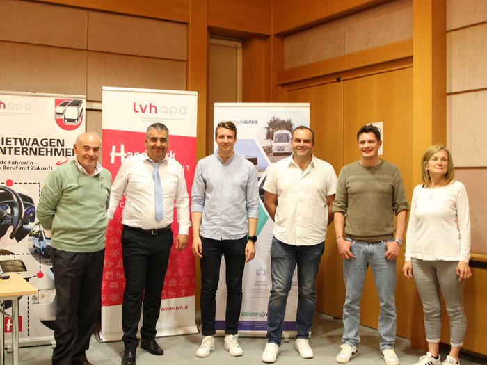 Autonoleggiatori e imprese Taxi in Alto Adige: lavorare insieme per migliorare le condizioni quadro Sei persone posano davanti a striscioni promozionali in una sala conferenze