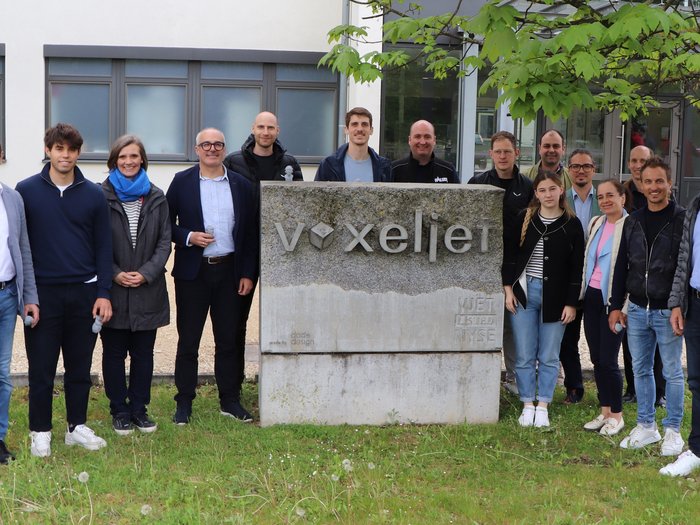 Ingegneria meccanica e impiantistica: imprenditrici e imprenditori altoatesini in viaggio d’affari ad Augusta Foto di gruppo davanti al cartello aziendale Voxeljet all'esterno