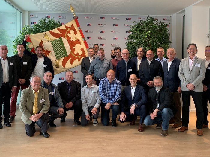 VEUKO-Kongress der Hafner/innen: Für die Zukunft des Kachelofens in Europa Gruppenfoto von Männern in Businesskleidung mit Fahne und Pflanzen im Hintergrund