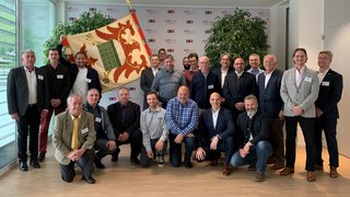 News Gruppenfoto von Männern in Businesskleidung mit Fahne und Pflanzen im Hintergrund