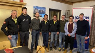 News Gruppe von acht Männern in einem Raum mit Tischen und Bannern im Hintergrund.