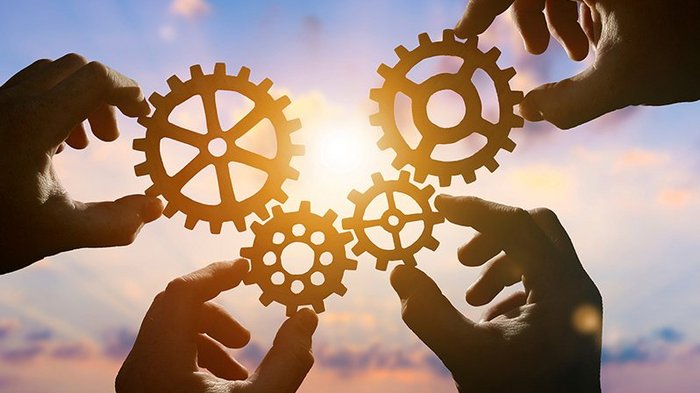 Digilog in die Zukunft Hände halten Zahnräder vor dem Sonnenuntergang, Symbol für Zusammenarbeit
