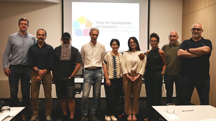 Südtiroler Handwerk setzt starkes Signal für Fachkräftegewinnung:  Erster territorialer Zusatzvertrag für den Bereich Körperpflege unterzeichnet Gruppenfoto von zehn Personen vor Leinwand mit Logo Haus der Sozialpartner Handwerk