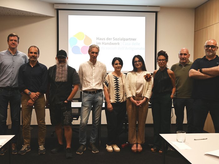 Südtiroler Handwerk setzt starkes Signal für Fachkräftegewinnung: Erster territorialer Zusatzvertrag für den Bereich Körperpflege unterzeichnet Gruppenfoto von zehn Personen vor Leinwand mit Logo Haus der Sozialpartner Handwerk