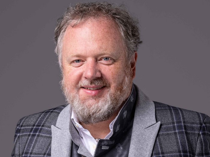 Für mehr Sicherheit am Arbeitsplatz/Lanz: „Mehr beraten und weniger strafen!“ Porträt eines lächelnden Mannes mit Bart und kariertem Sakko vor grauem Hintergrund